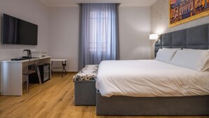 Une chambre d’hôtel moderne avec un grand lit, un bureau doté d’un téléviseur à écran plat, une machine à café et un tableau au mur.