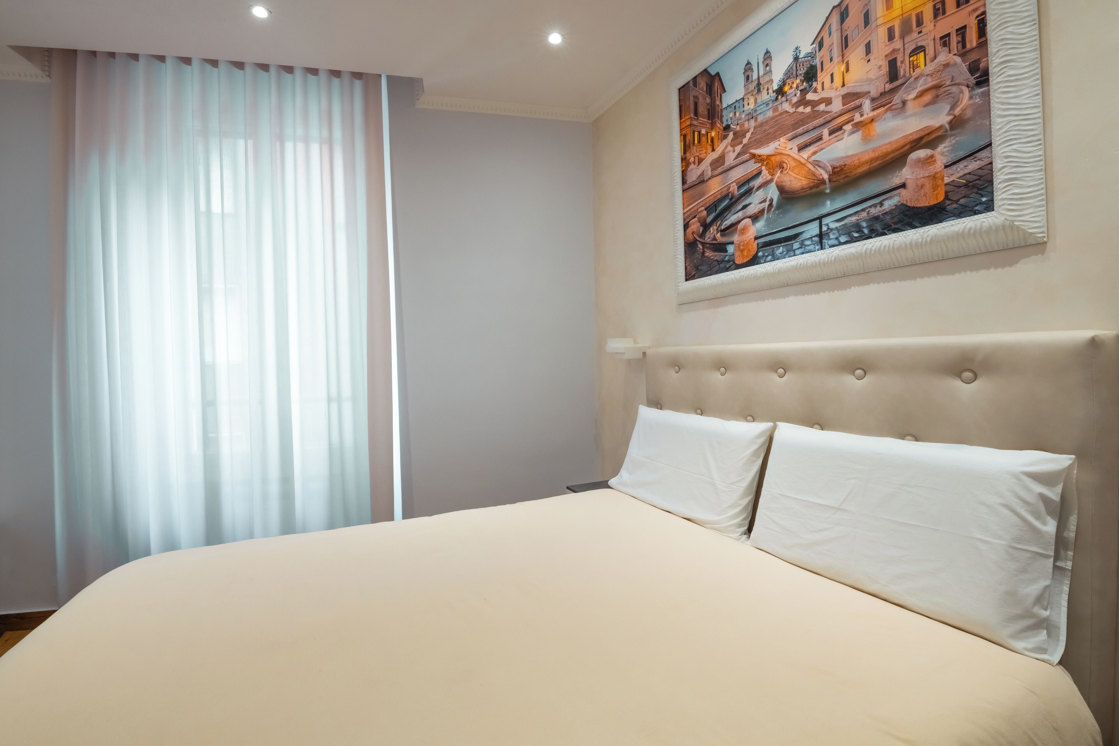 Una habitación de hotel con una cama grande, un cabecero con diseño capitonado y un cuadro de un paisaje urbano en la pared.