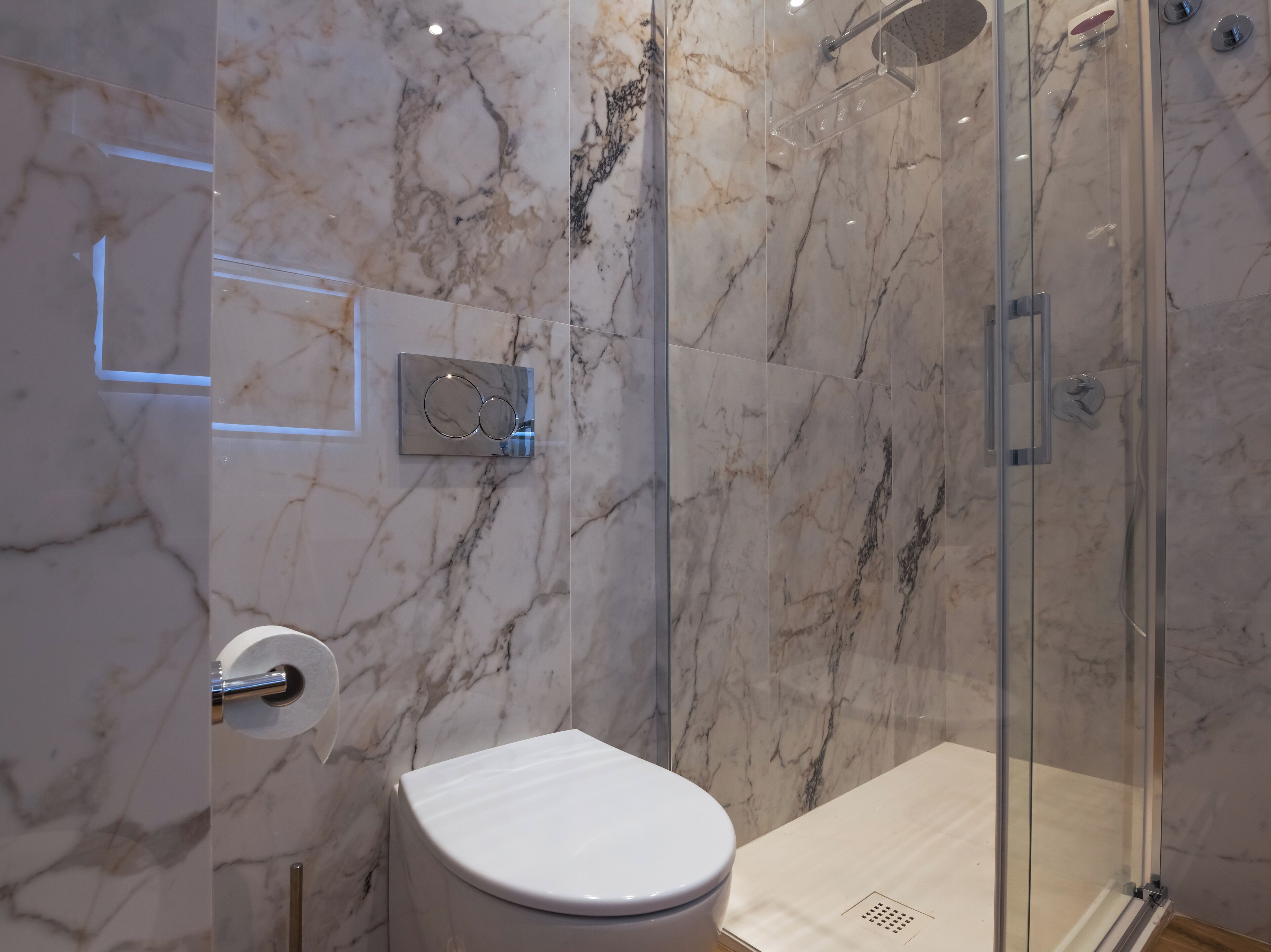 Un baño con inodoro, cabina de ducha de vidrio y paredes de mármol.