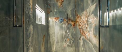 A modern bathroom with a marble wall, a shower, and a mirror.