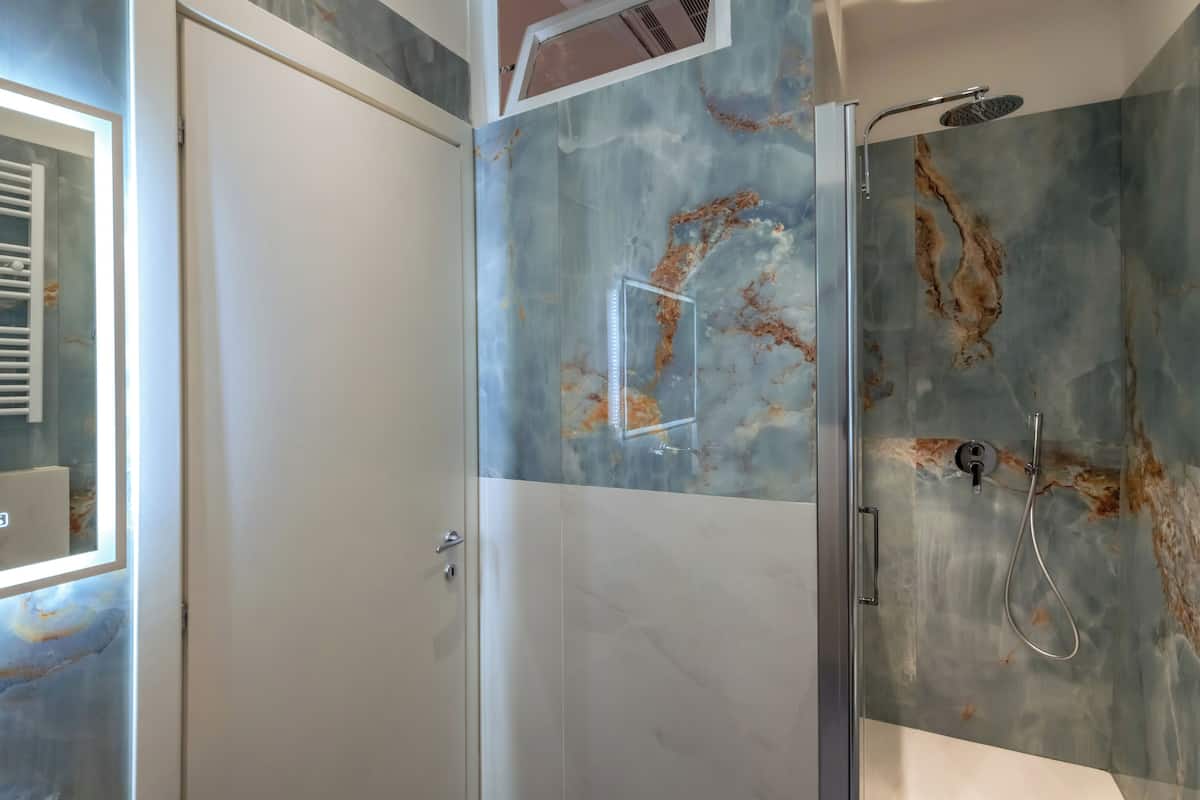 A bathroom with a glass shower enclosure, a white door, and a marble wall with a unique pattern.