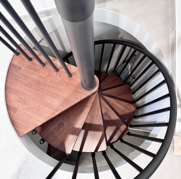 A spiral staircase with a copper-colored handrail and black balusters.