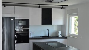 A modern kitchen with a central island, stainless steel appliances, and a window providing natural light. - Holiday house in northern dalmatia (Zadar)