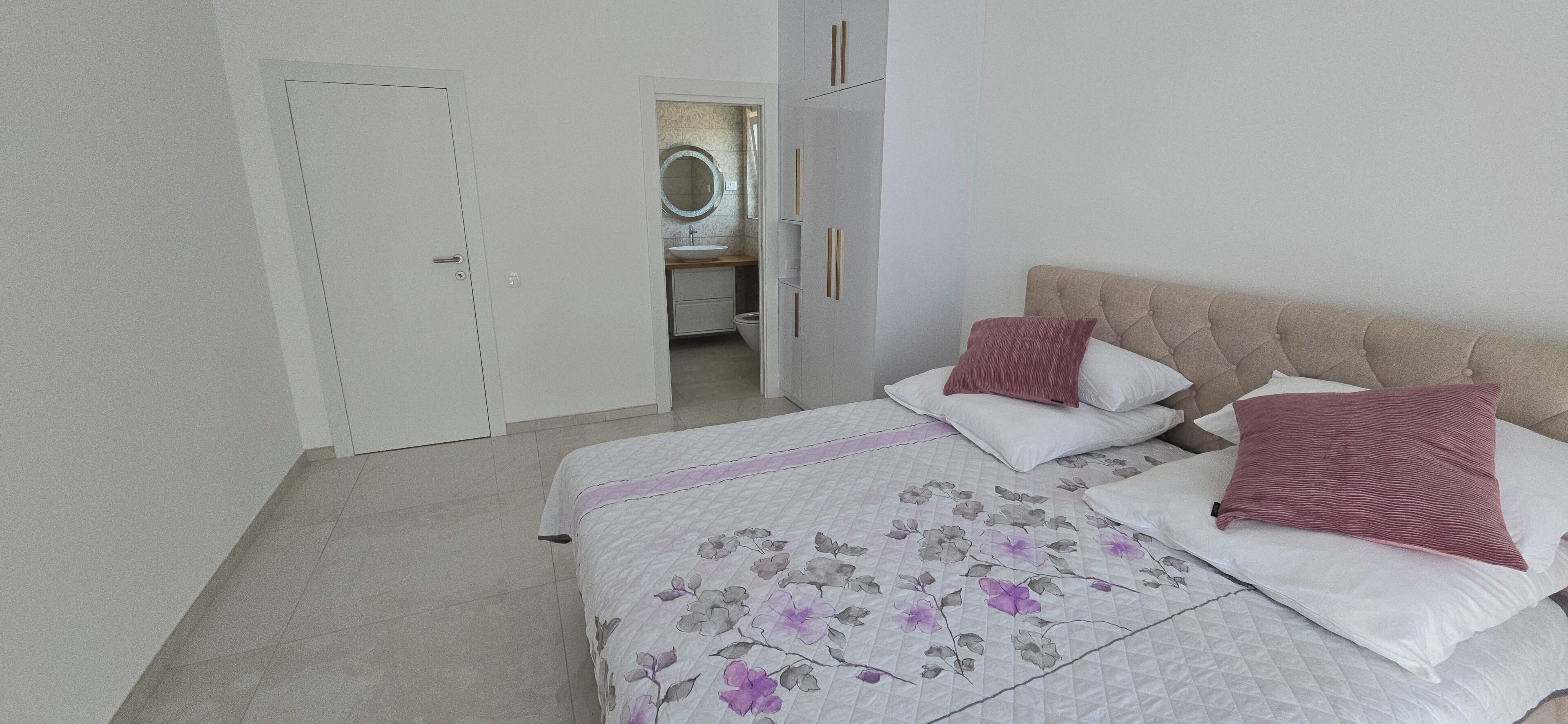 Un dormitorio con cama, almohadas, una mesita de noche y una puerta que da a un baño.
