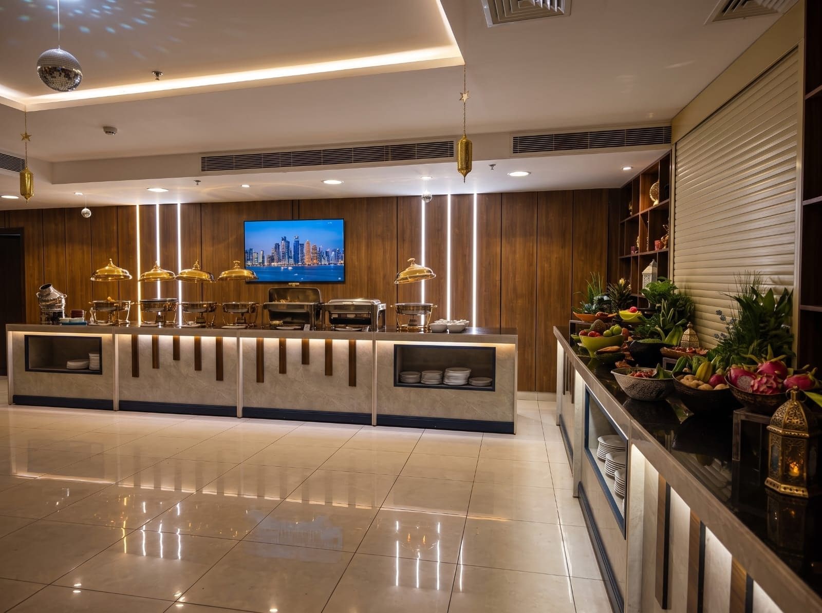 A hotel reception area with a modern design, featuring a flat-screen TV, buffet counter, and decorative plants.