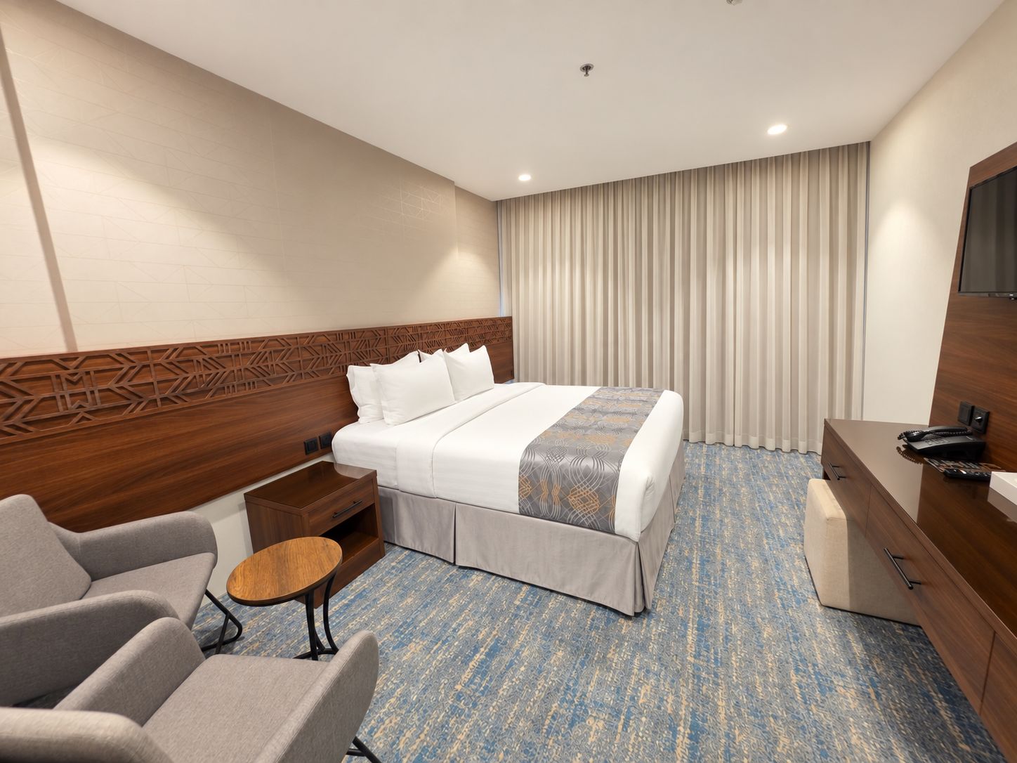 A hotel room with a bed, a desk, a chair, a small table, and a television.