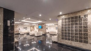 Un moderno vestíbulo de hotel con un suelo limpio y reflectante, zonas de estar blancas y una pared decorativa con patrones geométricos.