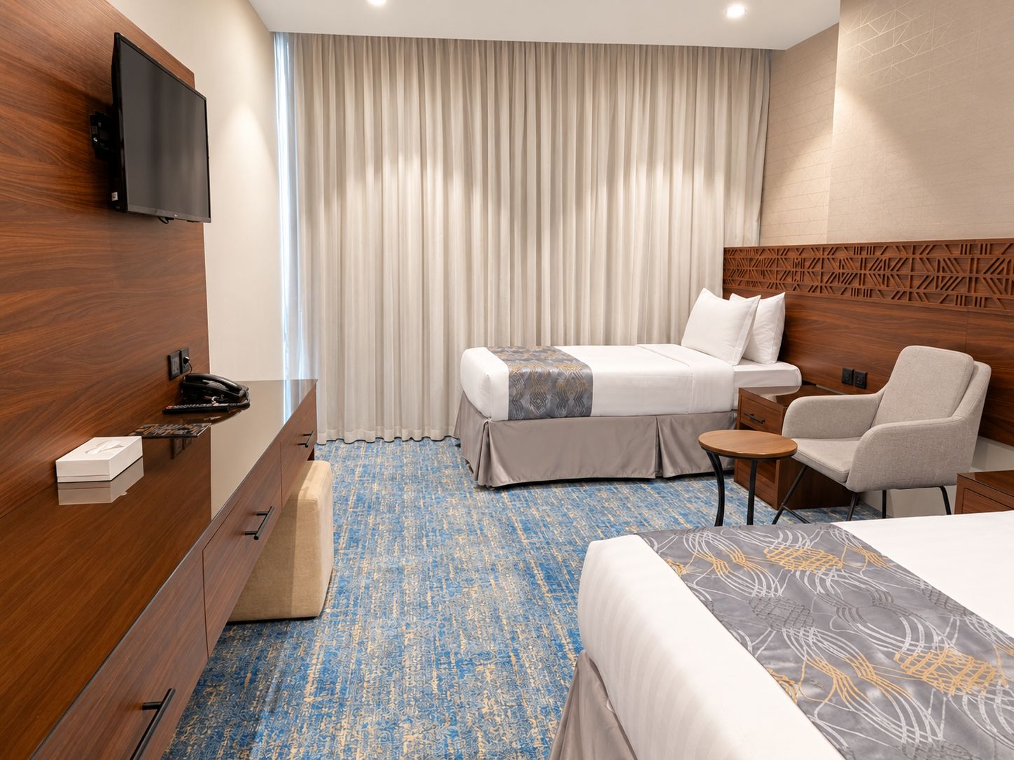 A hotel room with a bed, a desk, a chair, a TV, and a curtain.