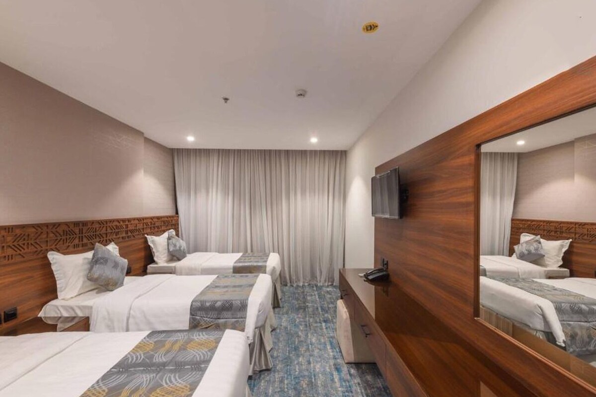 A hotel room with three beds, a wooden headboard, a mirror, and a flat-screen TV.