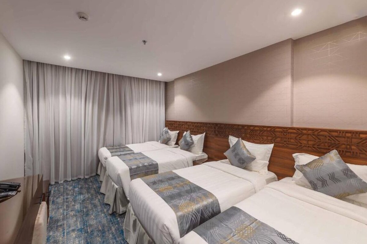 A hotel room with three beds, a wooden headboard, a large window with curtains, and a blue patterned carpet.