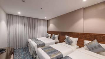 Ein Hotelzimmer mit drei Betten, einem Holzkopfende, einem großen Fenster mit Vorhängen und einem blau gemusterten Teppich.