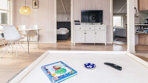 En moderne stue med spiseplads, fjernsyn og reol.