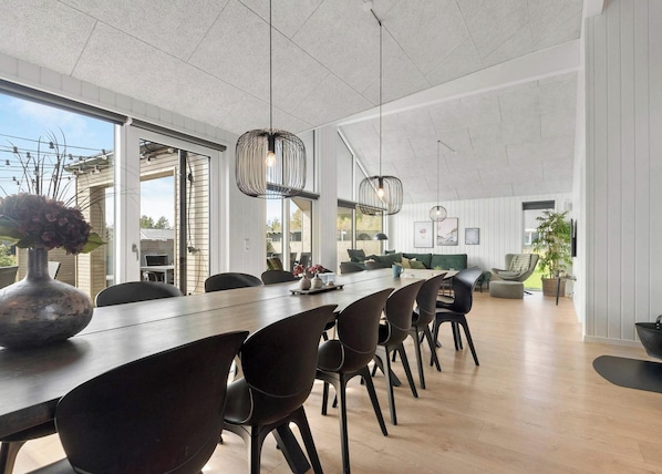 A modern dining area with a long table, black chairs, and pendant lights. - 5 Star Holiday Home in Norre Nebel (Norre Nebel)
