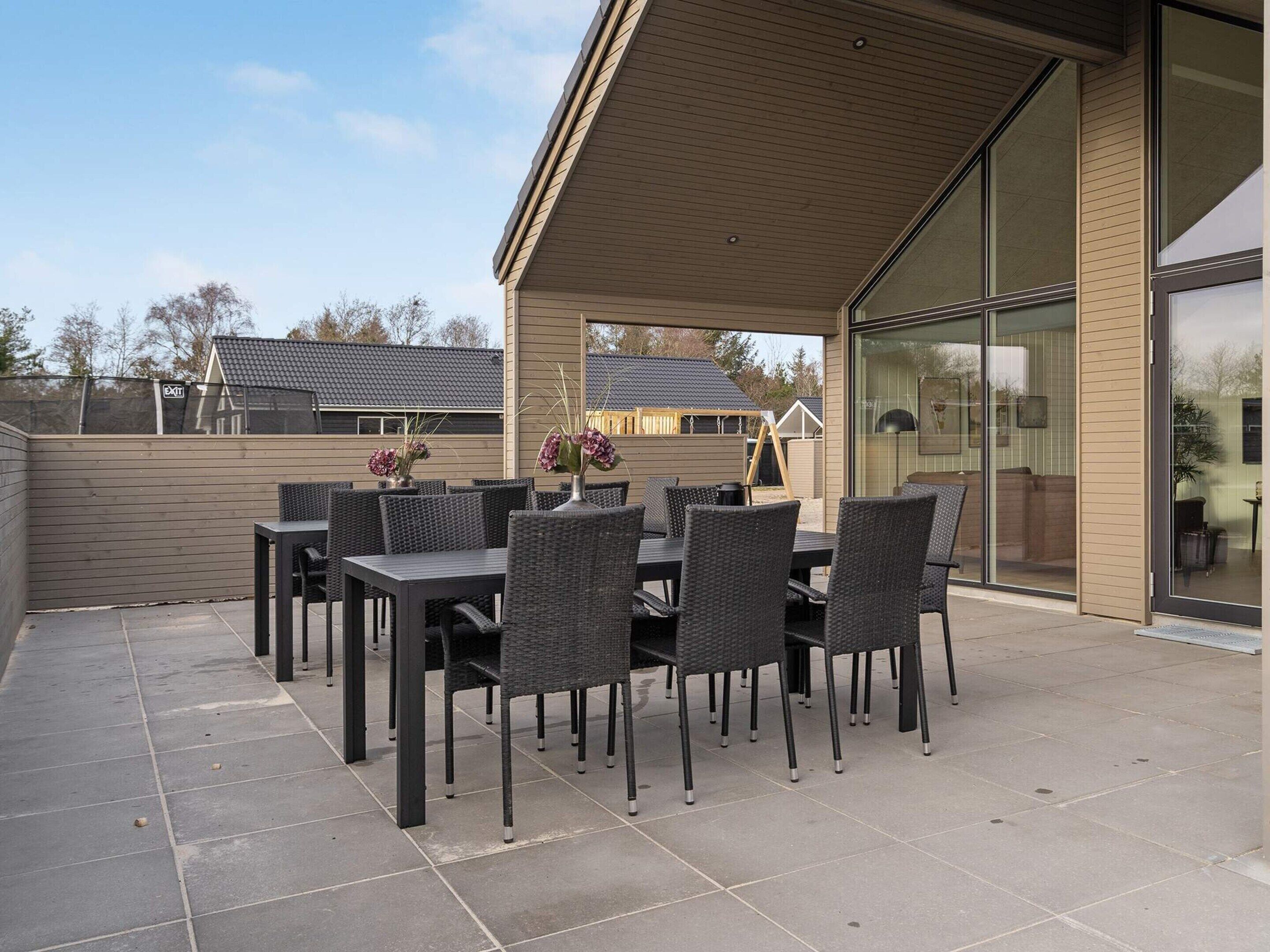 An outdoor patio with a covered seating area, featuring a table and chairs, and a view of the adjacent building.