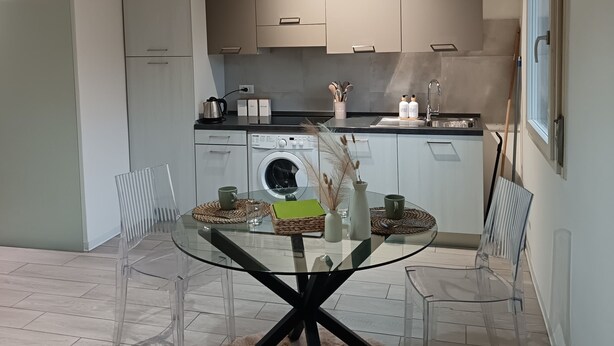 A modern kitchen with a dining area, including a glass table, chairs, and a hanging light fixture. - Little house in Padua, close to the center and very convenient to the major concerts in Padua (Padova)
