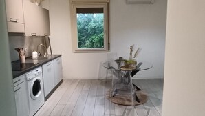 A compact kitchen with a washing machine, a dining table with chairs, and a window with a view of greenery. - Little house in Padua, close to the center and very convenient to the major concerts in Padua (Padova)