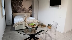A compact living space with a bed, a dining table with chairs, a TV mounted on the wall, and a ceiling light fixture. - Little house in Padua, close to the center and very convenient to the major concerts in Padua (Padova)