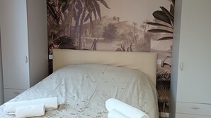 A bedroom with a floral bedspread, two rolled towels, and a tropical mural on the wall. - Little house in Padua, close to the center and very convenient to the major concerts in Padua (Padova)