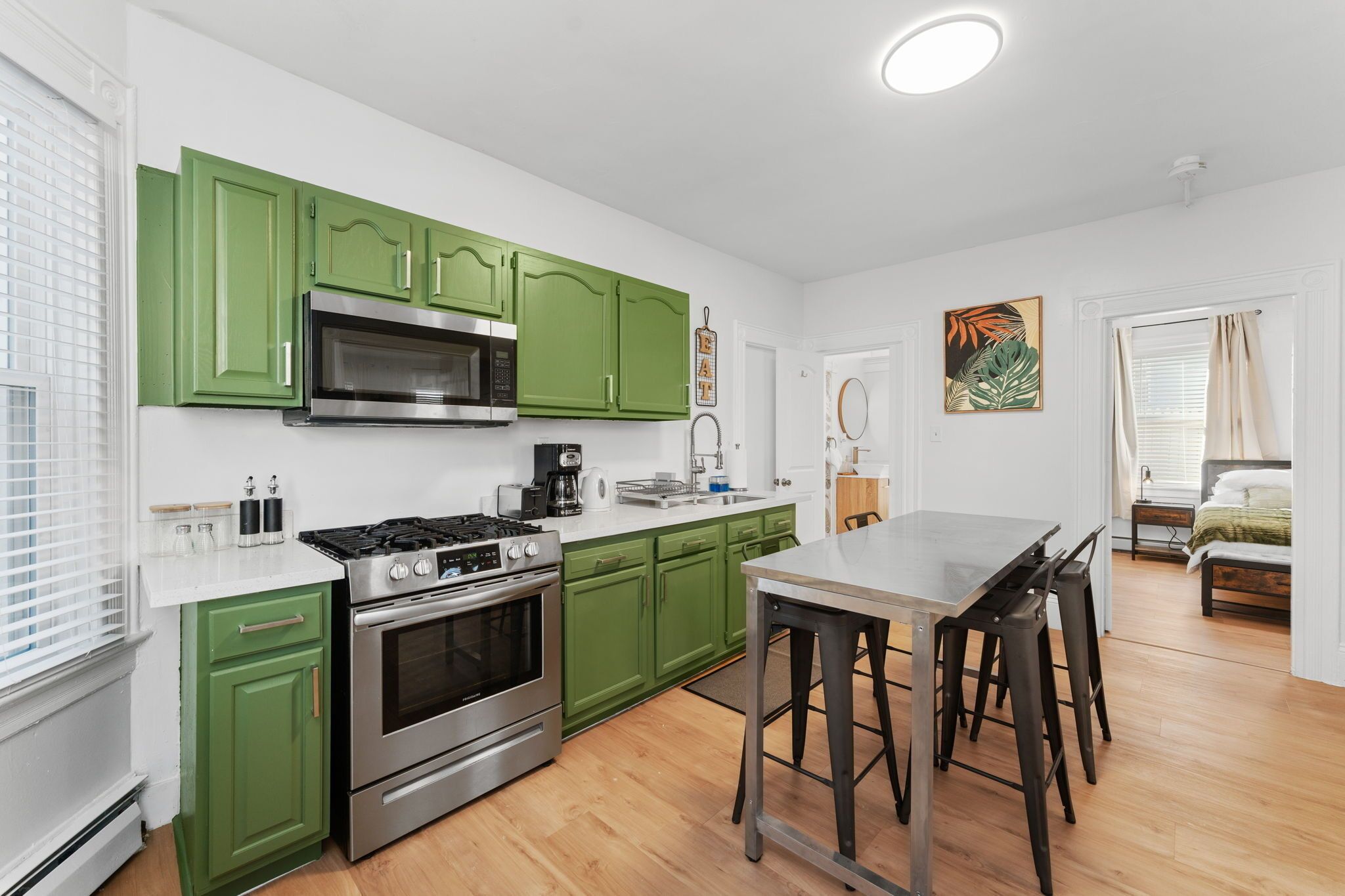 Une cuisine moderne avec des meubles de couleur verte, une cuisinière en acier inoxydable et un plan de travail blanc.