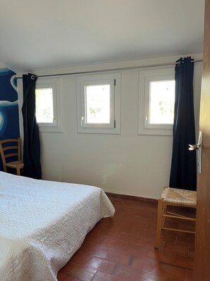 Een slaapkamer met een bed, twee ramen, een stoel en een deur.