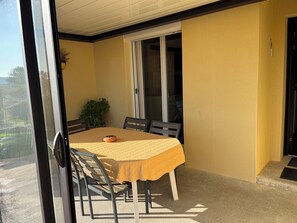Een balkon met een tafel, stoelen, een bloempot en een schuifdeur.