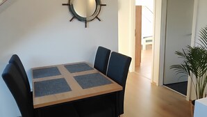 A dining area with a wooden table and chairs, a ship's wheel wall decoration, and a staircase leading to another room.