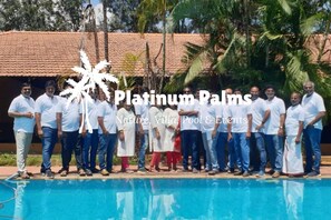 A group of people standing by a pool with a tropical backdrop. - Platinum Palms Villa With Pool (Anekal)