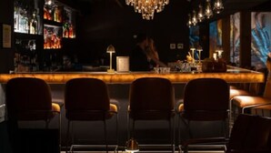 A bar area with a bar counter, chairs, a chandelier, and a bartender.