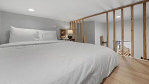 A bedroom with a large bed, a nightstand, a lamp, and a wooden beam structure.