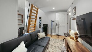 A modern living room with a sofa, a wooden ladder, a TV, and a door.
