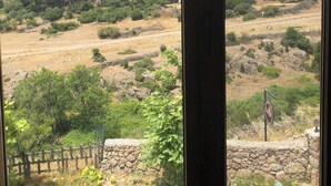 Vista a través de una ventana que muestra un paisaje con un muro de piedra, una cerca de madera y un letrero.