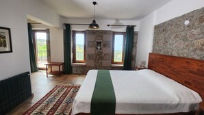 A bedroom with a large bed, a wooden headboard, a stone wall, and a view of the outdoors through a window. - Assos Pırnal Köy Evi  (Ayvacik)