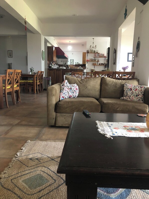 A living room with a sofa, coffee table, and a rug. There is a dining area with chairs and a table in the background. - Assos Pırnal Köy Evi (Ayvacik)