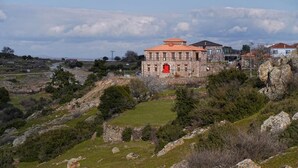 Un edificio de piedra con una puerta roja, rodeado por un paisaje montañoso y vegetación escasa.