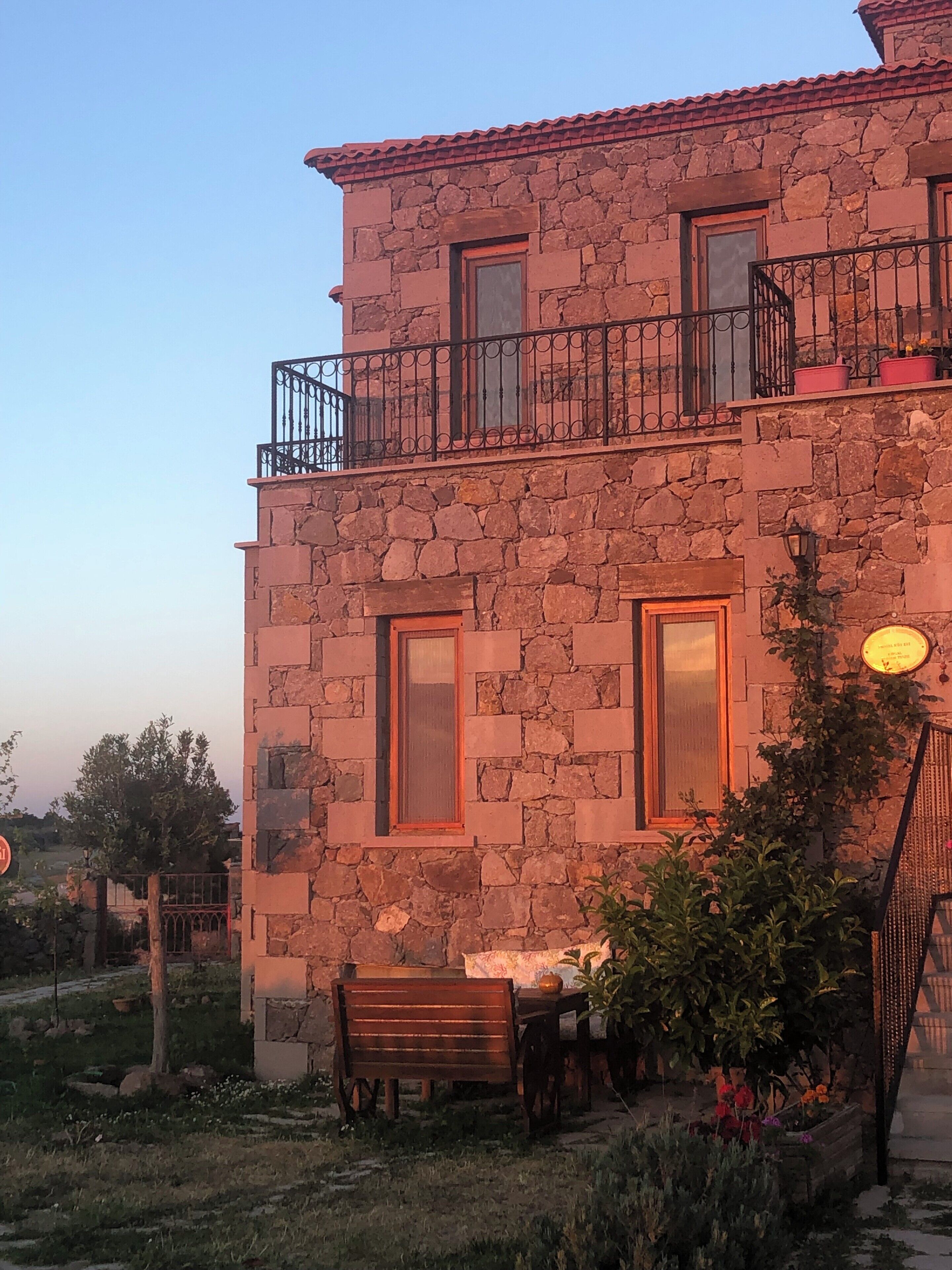 A stone building with a balcony, a table with chairs, and a bench.