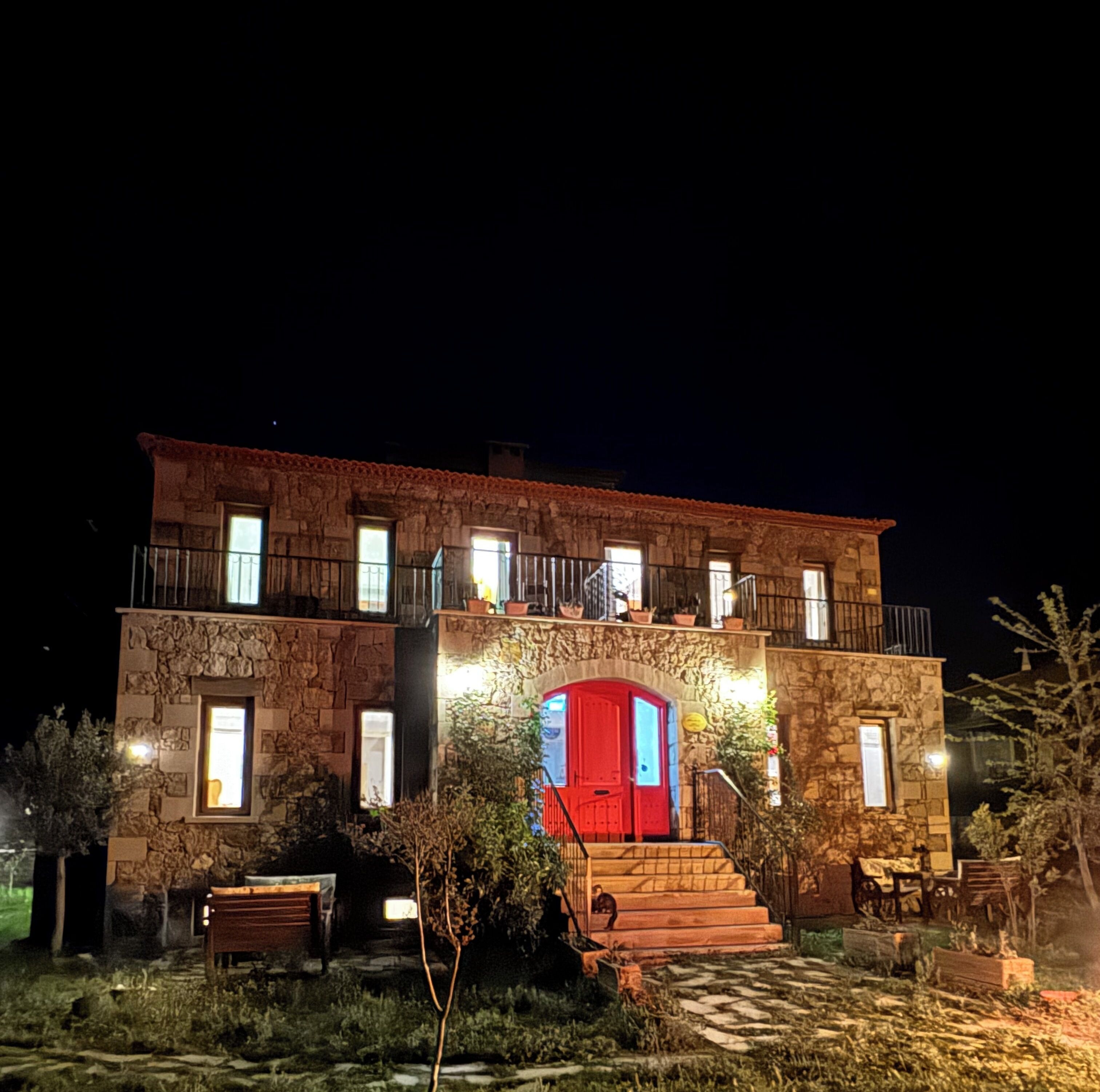 Ein zweistöckiges Steinhaus mit roter Tür und zahlreichen Fenstern.