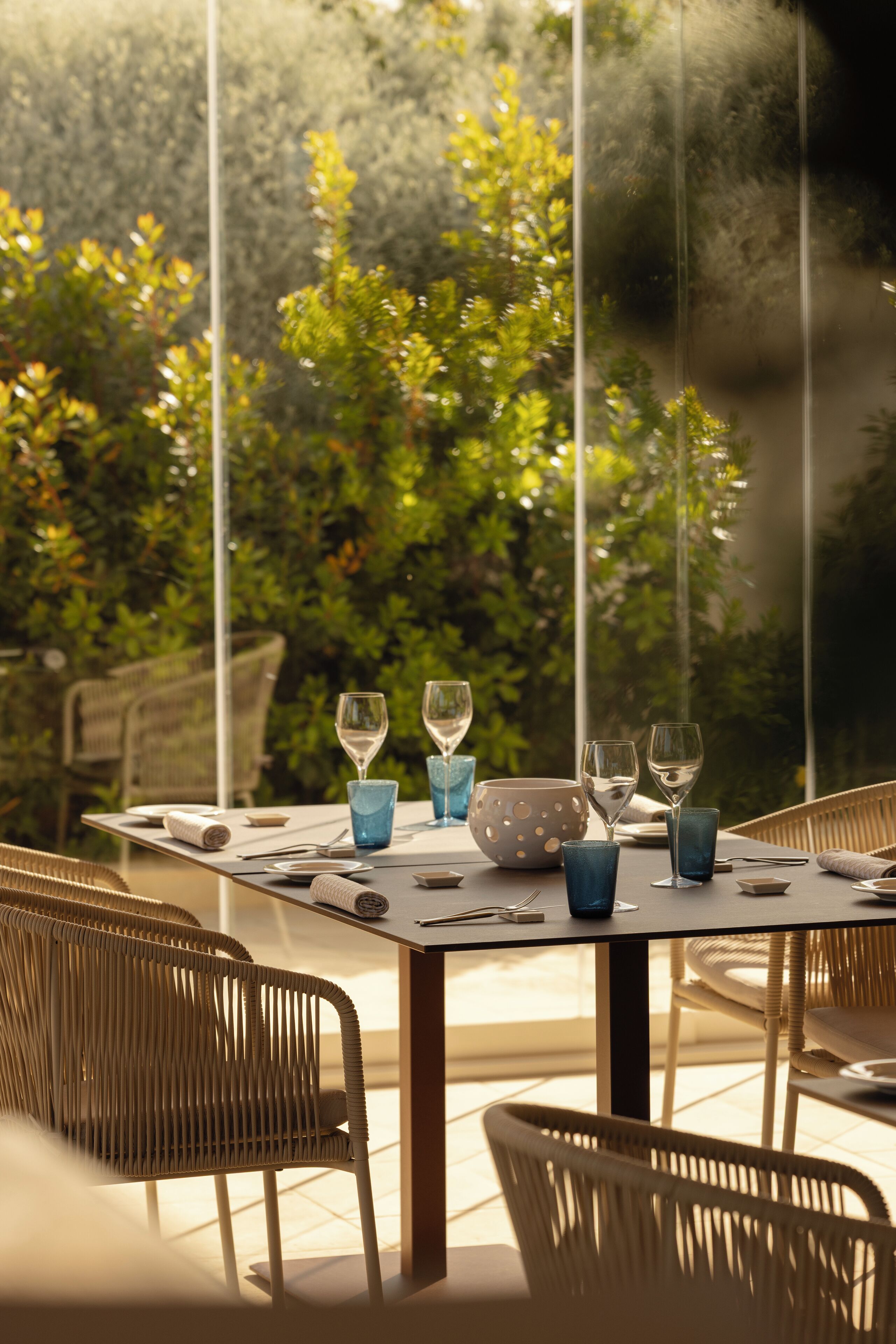 An outdoor dining area with wicker chairs and a table set with wine glasses, bowls, and cutlery.