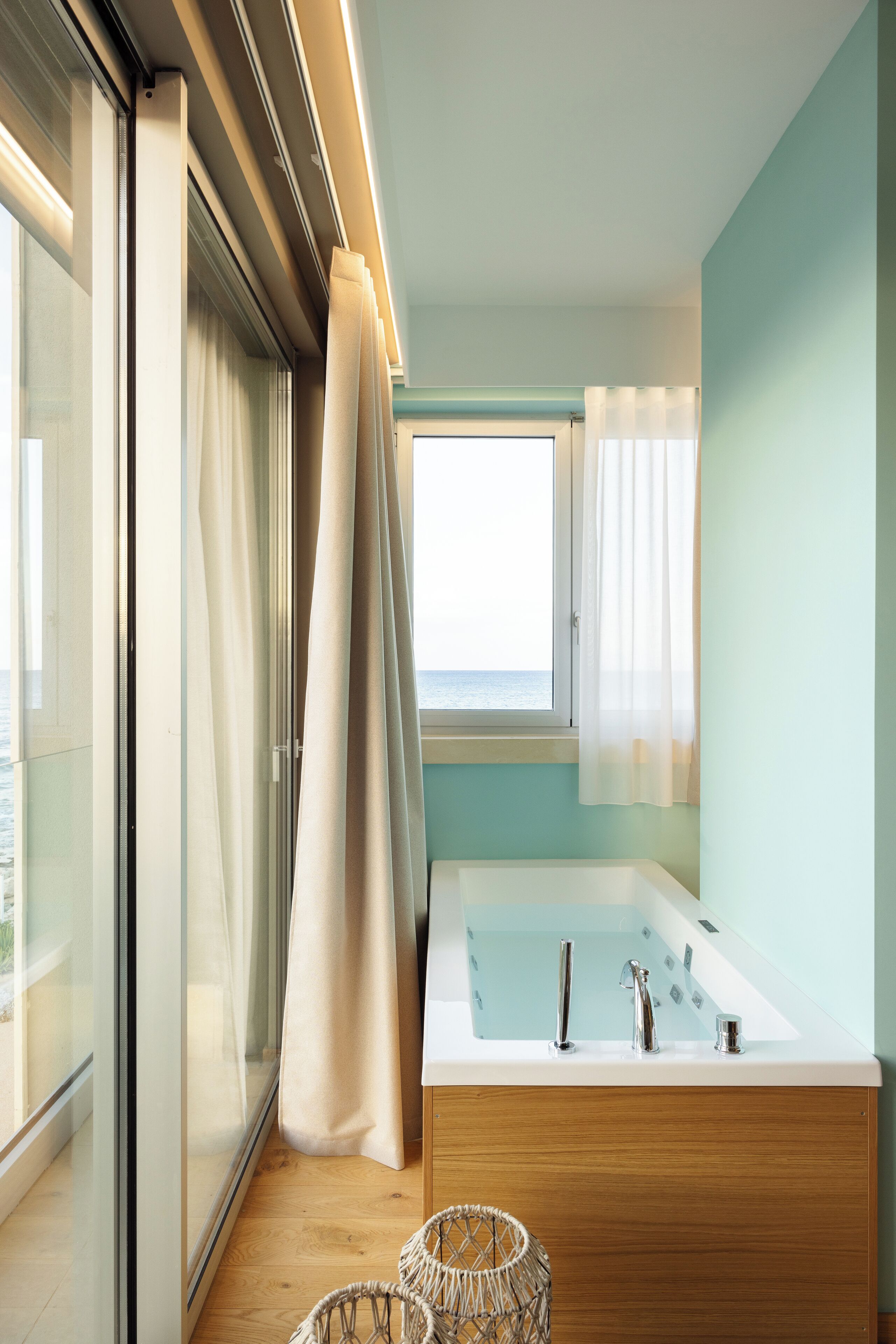 A modern bathroom with a large bathtub, a wooden vanity, and a view of the sea through a sliding glass door.