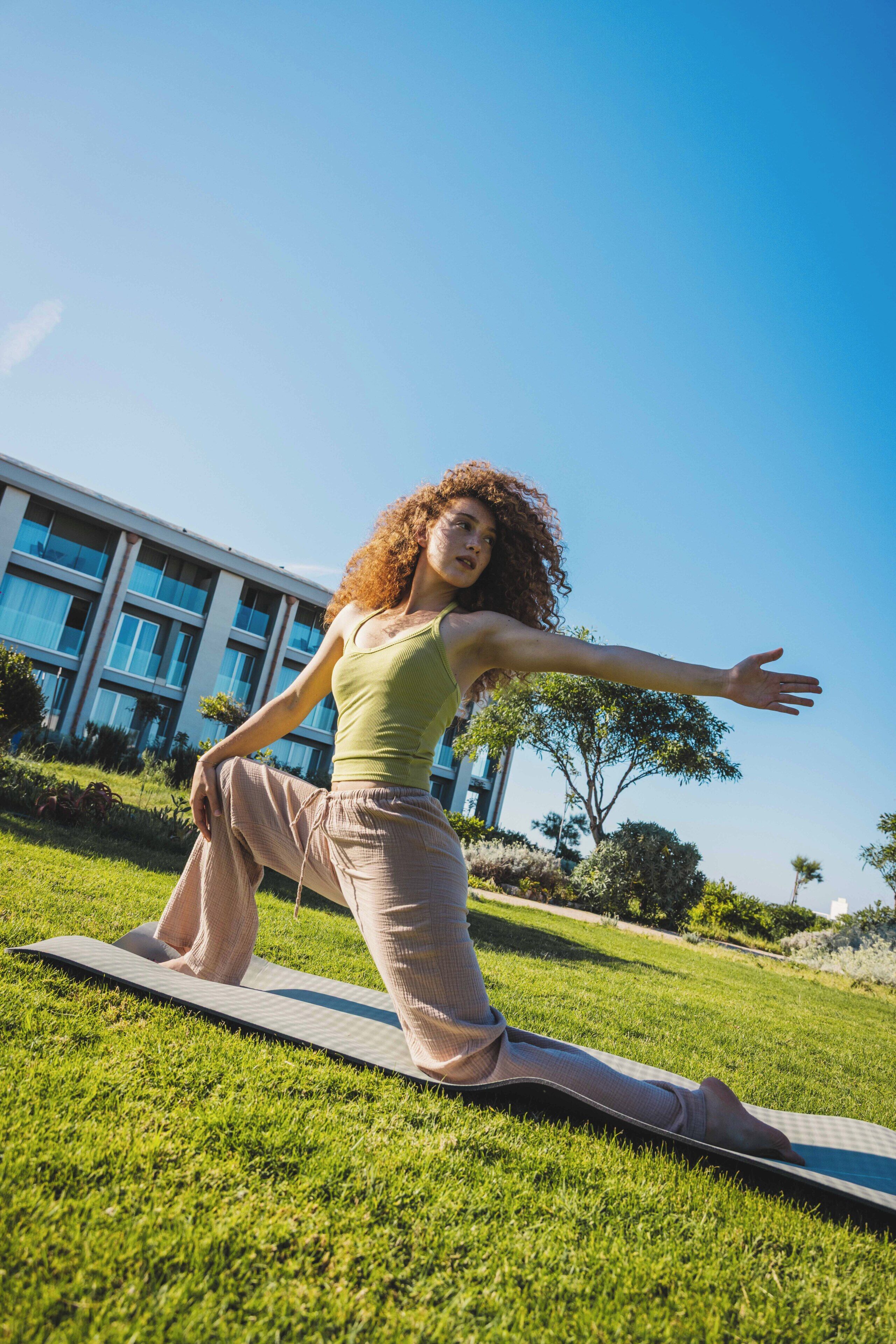 A person performing a yoga pose on a mat outdoors with a building in the background.