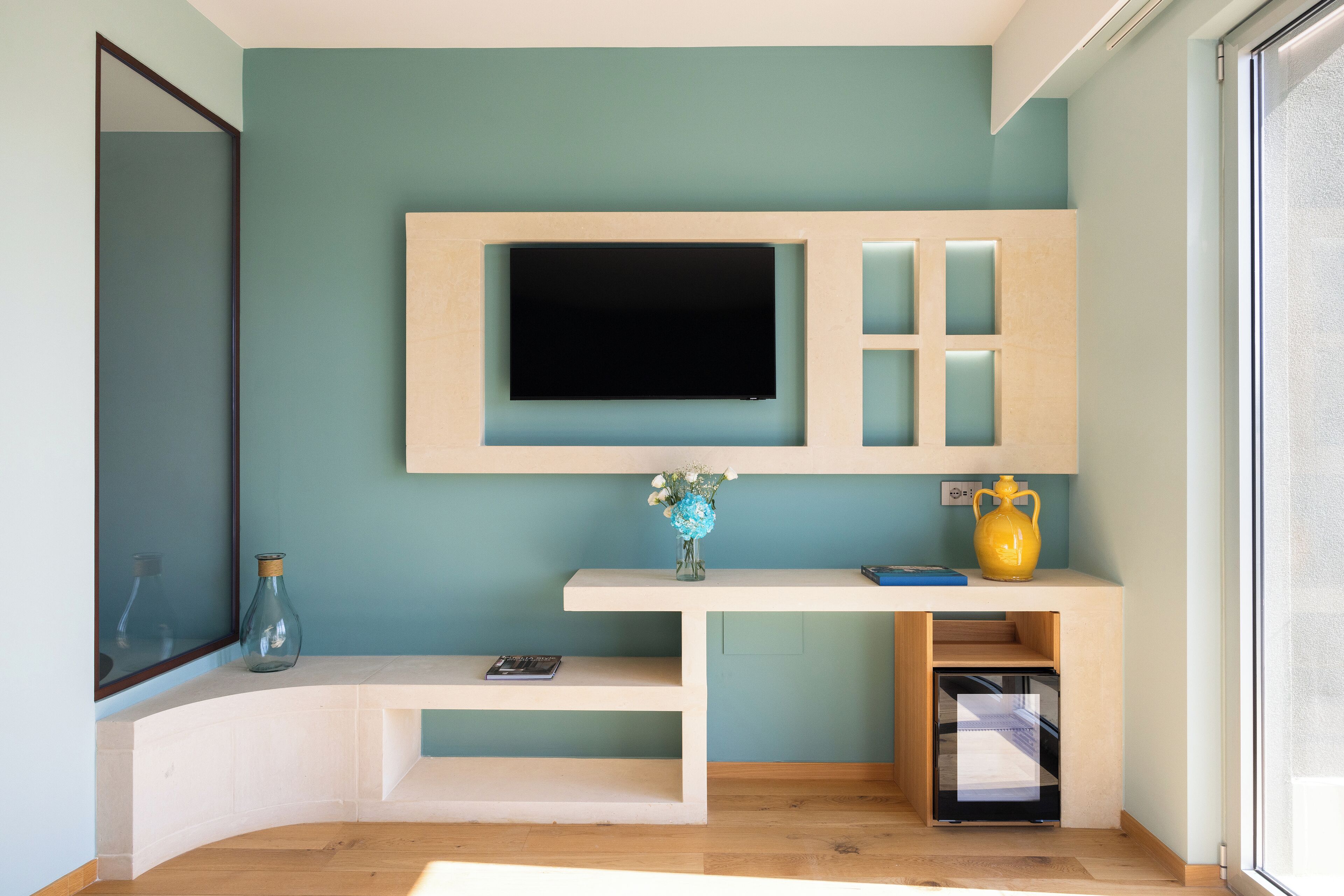 A modern living room with a flat-screen TV mounted on a wall, a small white console table with a vase of flowers, and a yellow vase on the console.