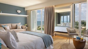 Habitación de hotel moderna con una cama grande, un sofá y una silla. Se ve el océano a través de amplios ventanales.