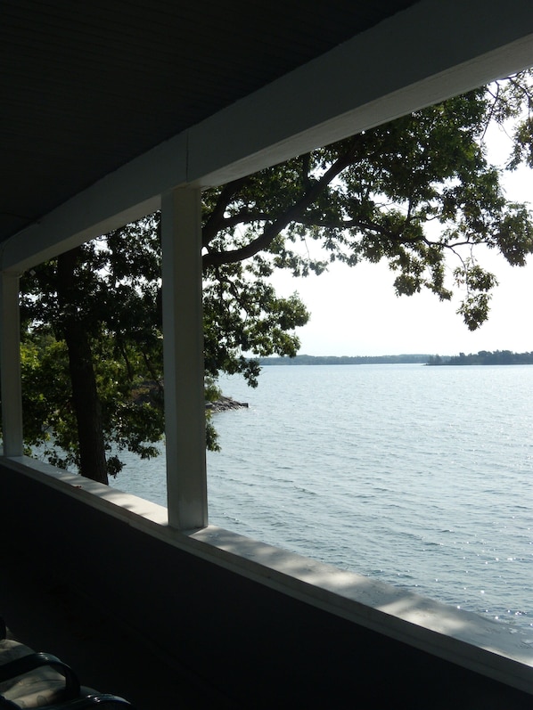 A view from a covered porch overlooking a calm body of water with trees in the foreground.