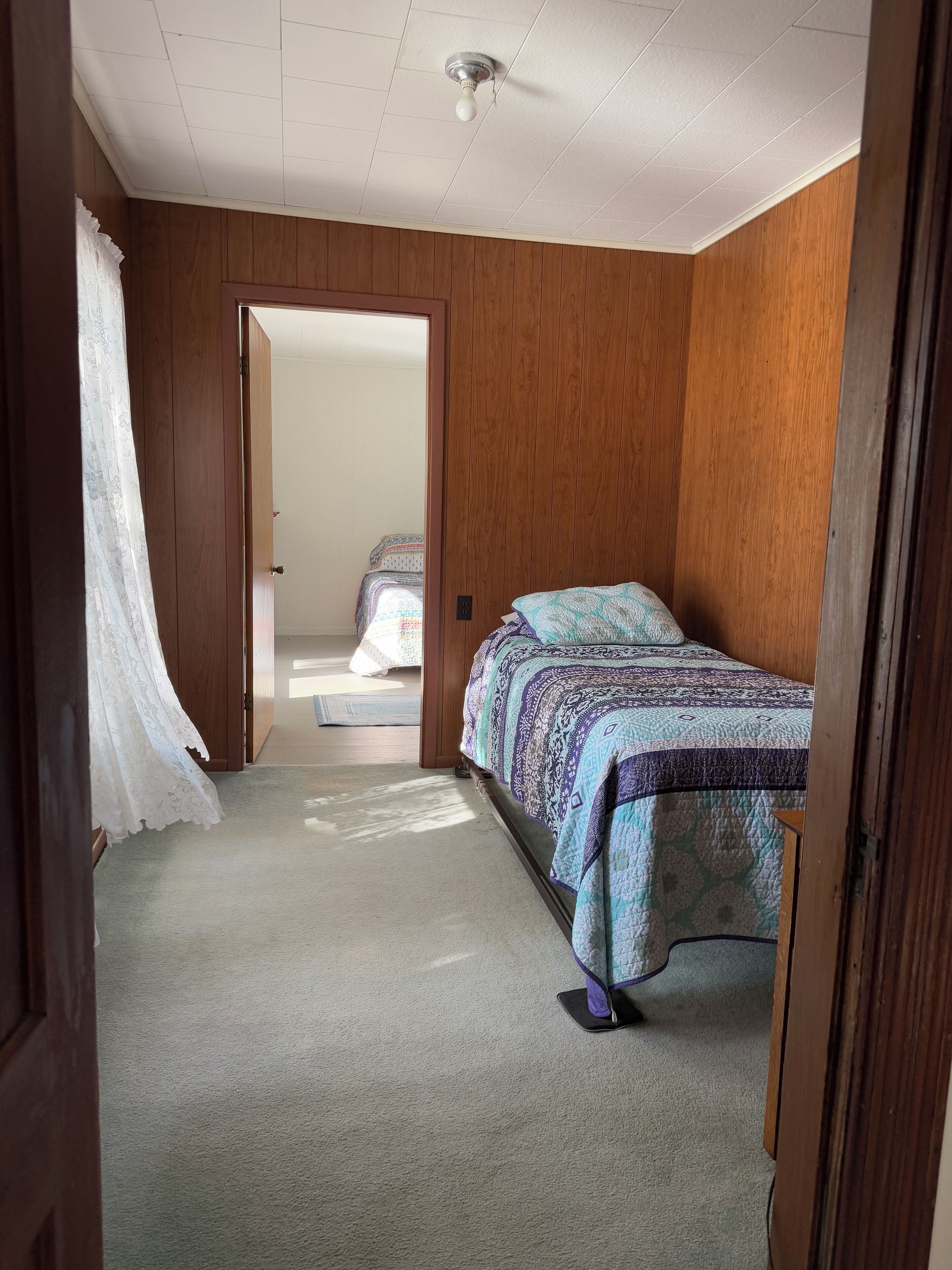 Une chambre avec un mur en bois, un lit recouvert d’une couvre-lit à motifs et un ventilateur de plafond.