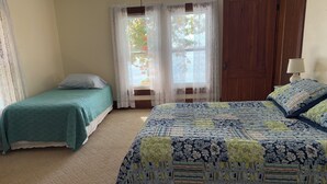 A bedroom with two beds, a wooden door, and a window with lace curtains. - Spacious Grindstone Island House across from Clayton, NY (Clayton)