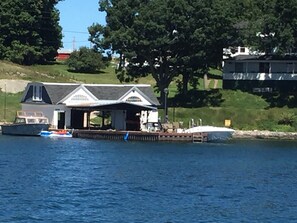 A docked boat near a house with a covered porch and a small dock extending into the water.