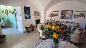 Una sala de estar con chimenea, un sofá, una mesa de centro con un jarrón de flores y una estantería.