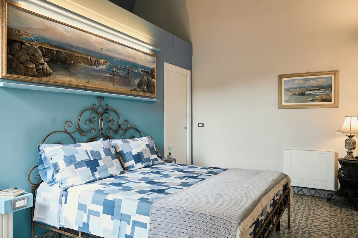 A bedroom with a bed, a nightstand, a dresser, a radiator, and a painting on the wall.