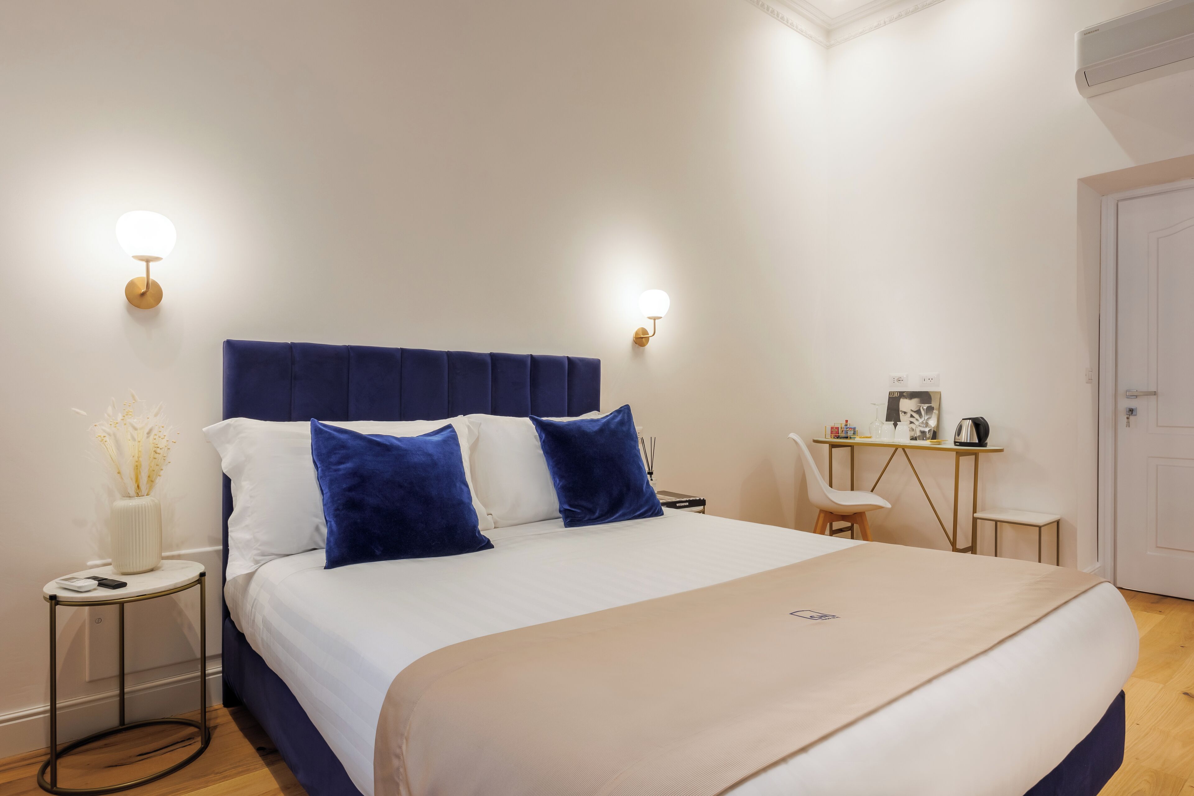 A neatly arranged bedroom with a large bed, bedside tables, a desk, and wall-mounted lights.