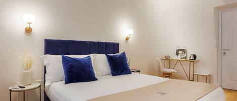 A neatly arranged bedroom with a large bed, bedside tables, a desk, and wall-mounted lights.