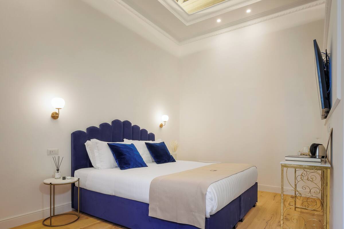 Un dormitorio con una cama grande, una mesita de noche pequeña, un televisor montado en la pared y un techo decorativo.